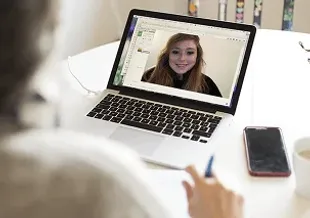 Person on a video call on a laptop, with a smartphone and cup on a table.
